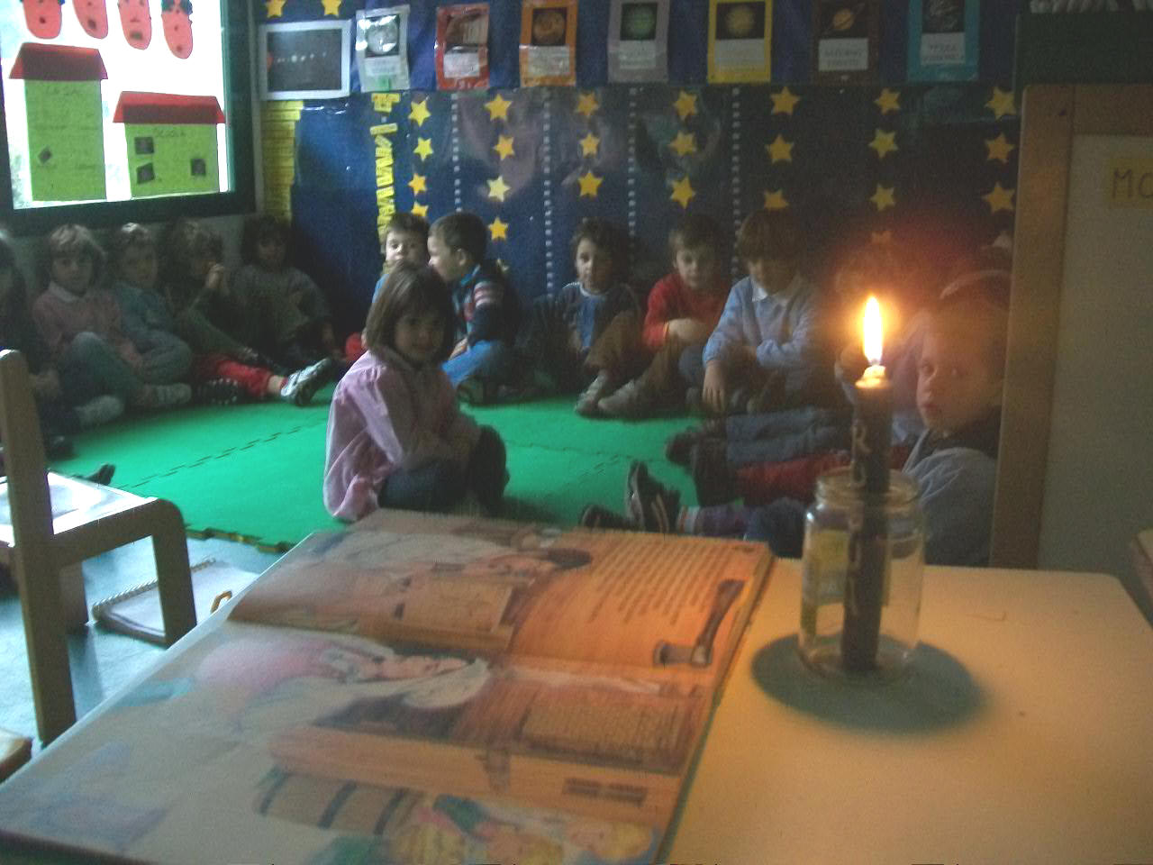 foto dei bambini che ascolatano la storia in cerchio con una candela accesa e luci spente