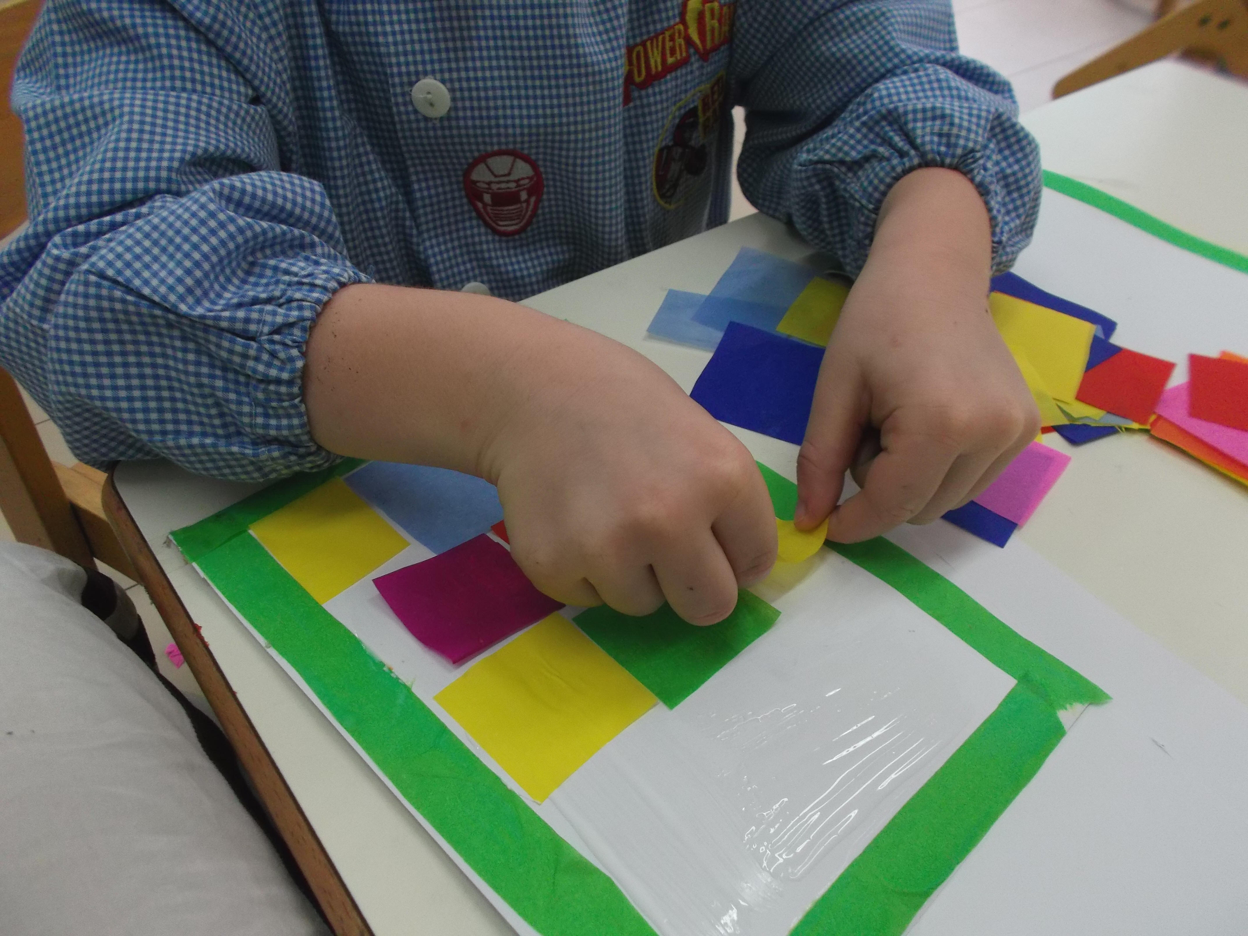 bambini che fanno collage con pezzettini di carta velina colorata per realizzare lo sfondo