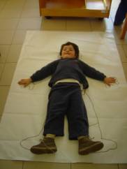 foto di un bambino disteso su un foglio che fa da modello per la sagoma del gigante 