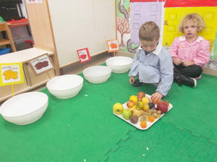 foto dei bambini che giocano  al gioco del colore  della frutta posizionandola nel corrispettivo contenitore del colore  del frutto scelto