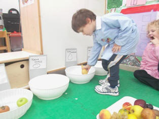 foto dei bambini che giocano  al gioco della forma della frutta posizionandola nel corrispettivo contenitore della forma del frutto scelto