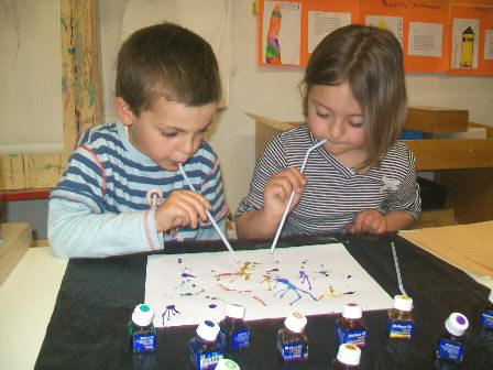 foto di bambini che pitturano soffiando con cannucce la china su di un foglio