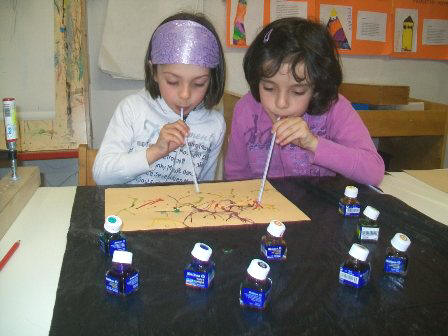foto di bambini che pitturano soffiando con cannucce la china su di un foglio